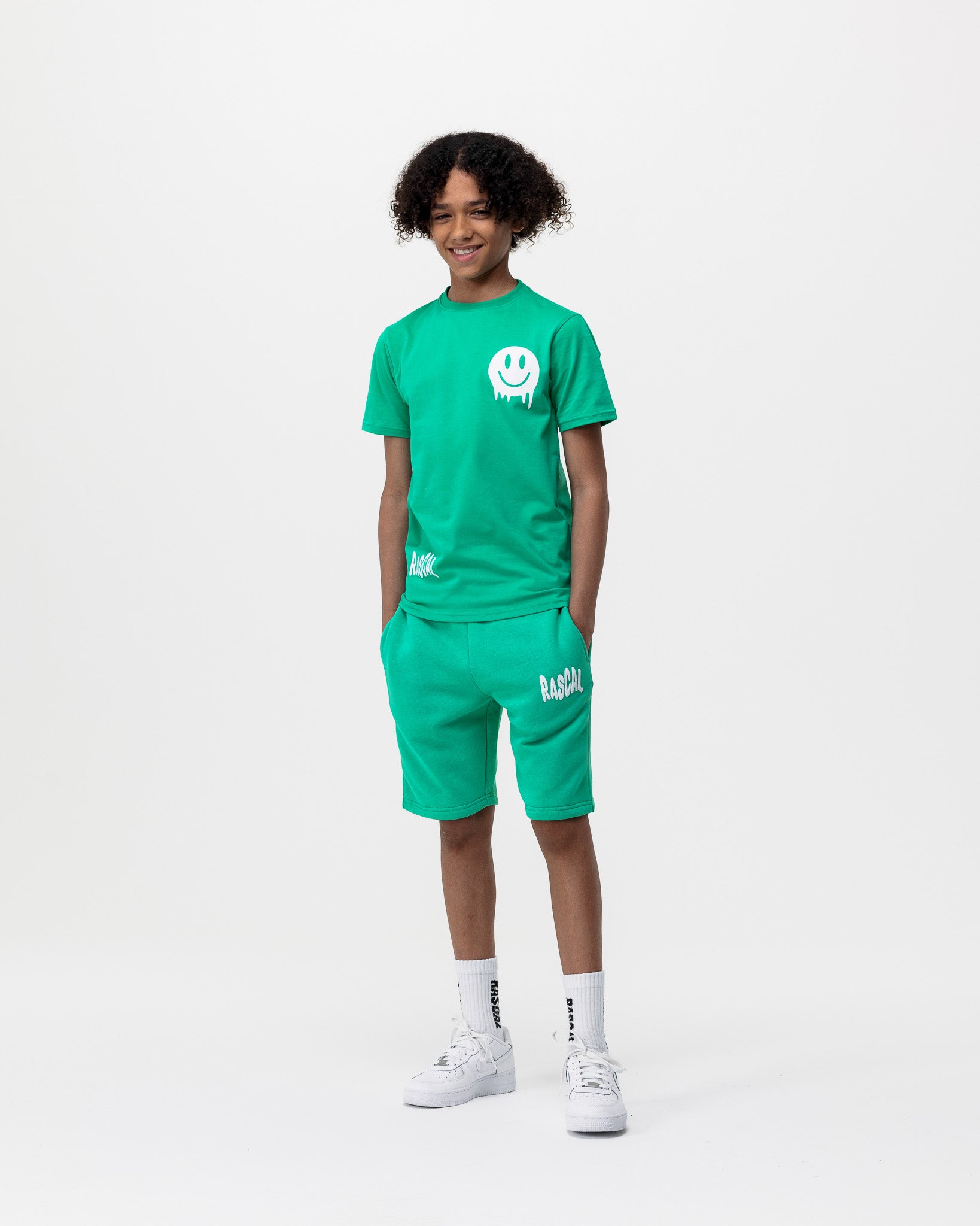 boy standing with hands in pockets wearing green Rascal shorts and Rascal green smiley face tshirt with white Rascal and smiley face graphics