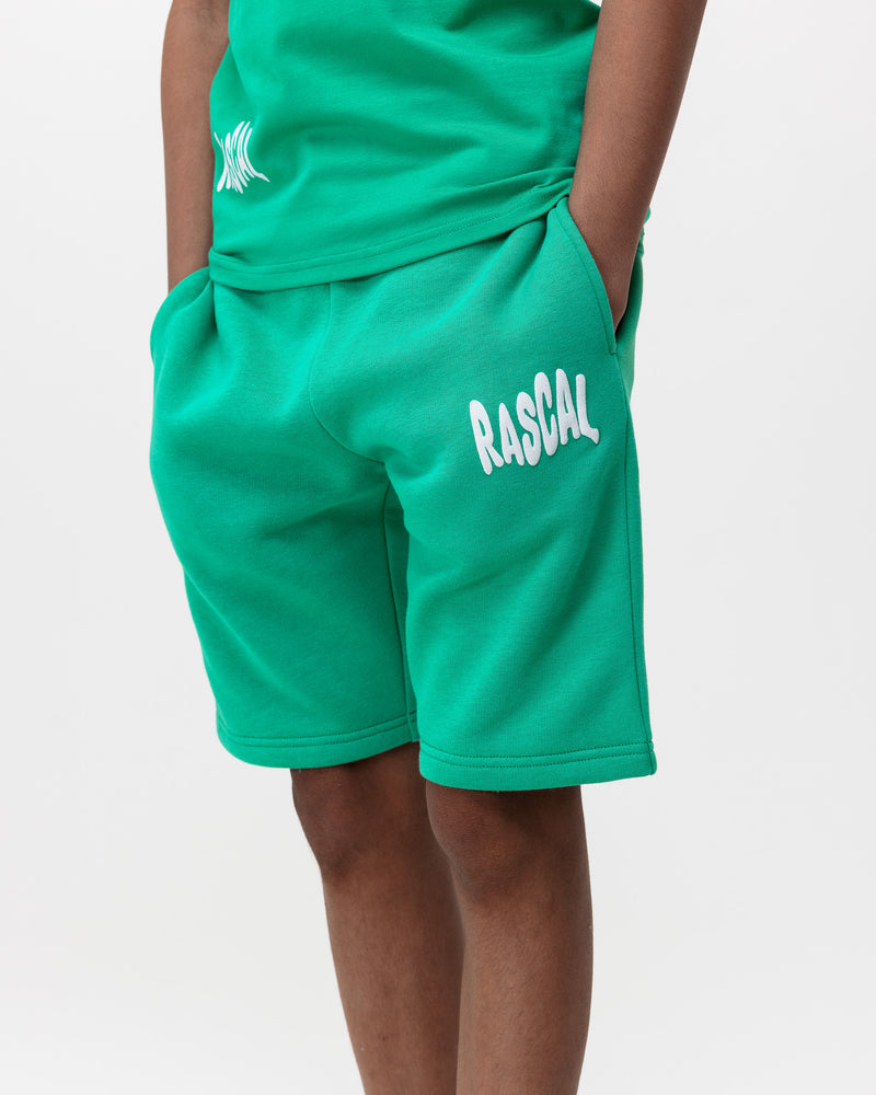 boy with hands in pockets wearing Rascal green kids cotton shorts with white Rascal logo graphic