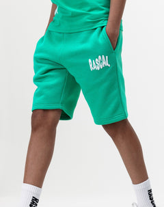 boy walking with hands in pockets wearing Rascal green kids cotton shorts with white Rascal logo graphic