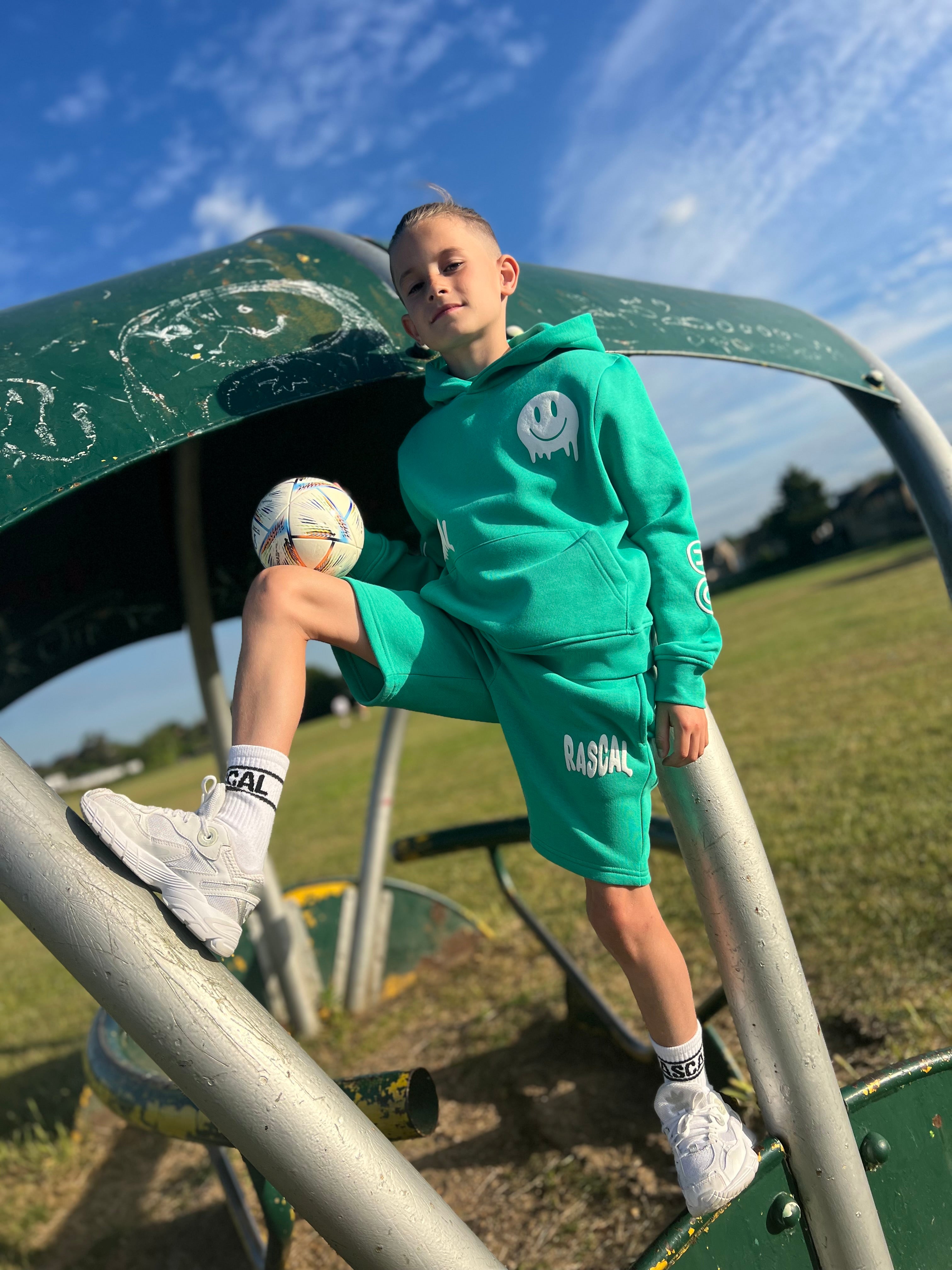 Roman Wingrove holding ball wearing Rascal green smiley hoodie and green kids cotton shorts with Rascal and smiley face graphics