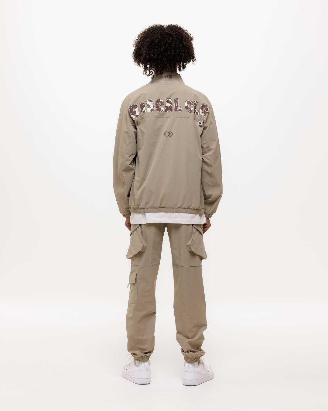 Boy wearing a Next Gen khaki jacket and cargos tracksuit with Rascal camo text printed on the back and other Rascal design elements