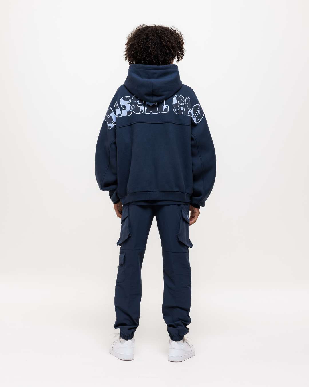 Boy wearing Next Gen junior navy blue cargo pants and hoodie tracksuit with Rascal camo text design on the back of the hoodie, standing against a white background