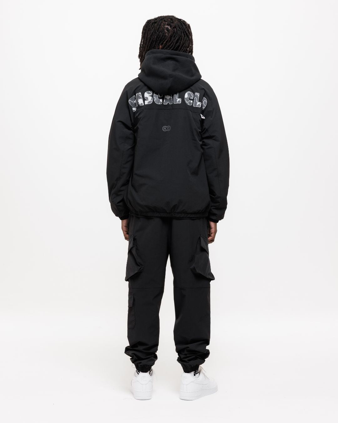boy wearing next gen black junior cargo pants and jacket with Rascal camo text designs on back of jacket, stood in front of a white background