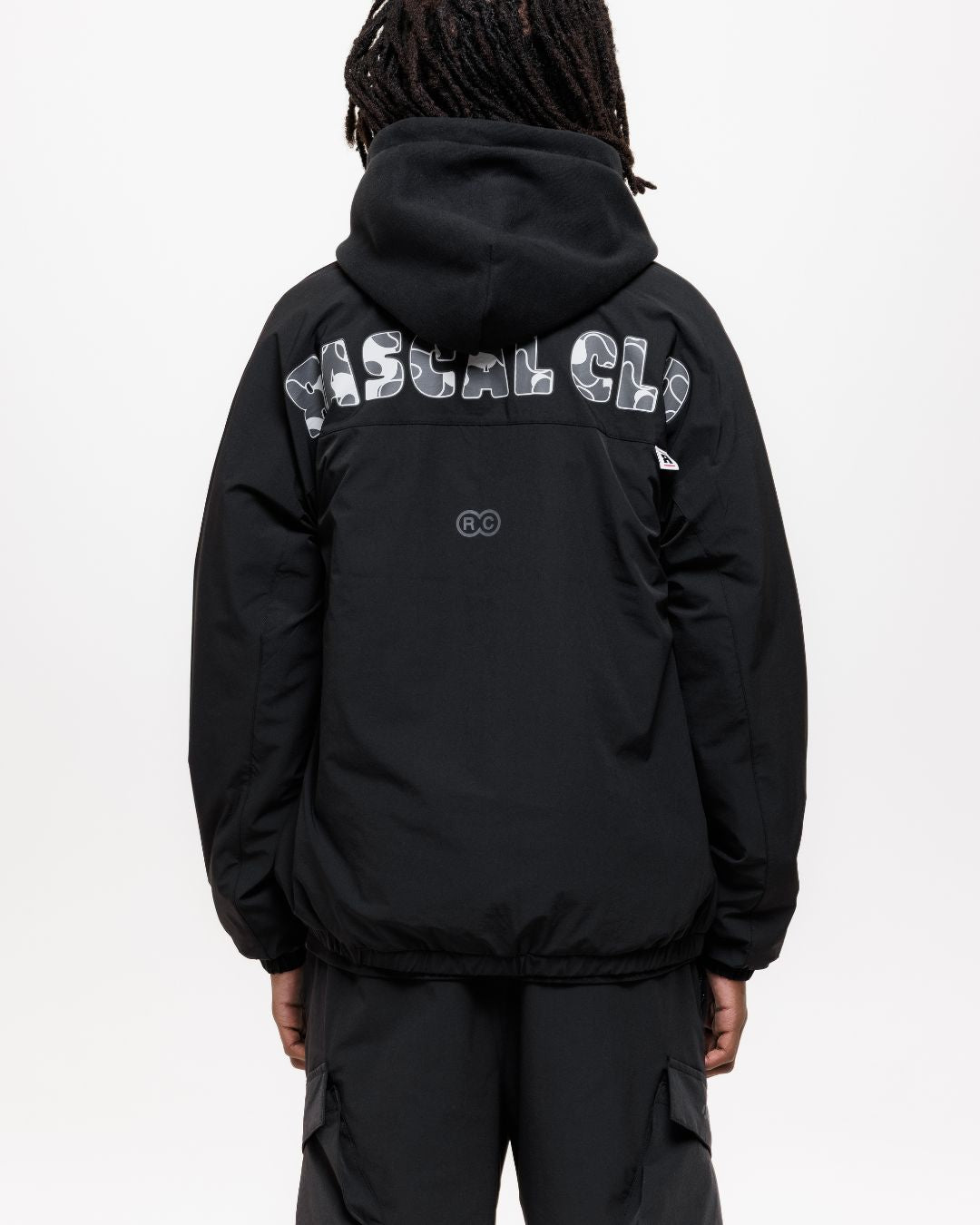 boy wearing next gen black junior shell jacket and cargo pants with Rascal camo text design on the back of jacket, stood in front of a white background