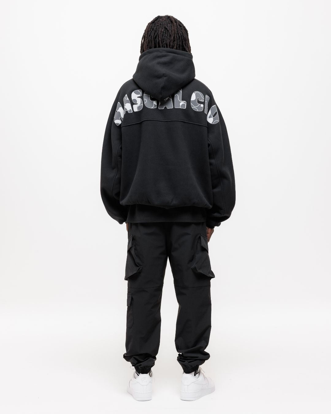 boy wearing next gen black junior oversized hoodie with Rascal camo text design and cargo pants stood in front of a white background