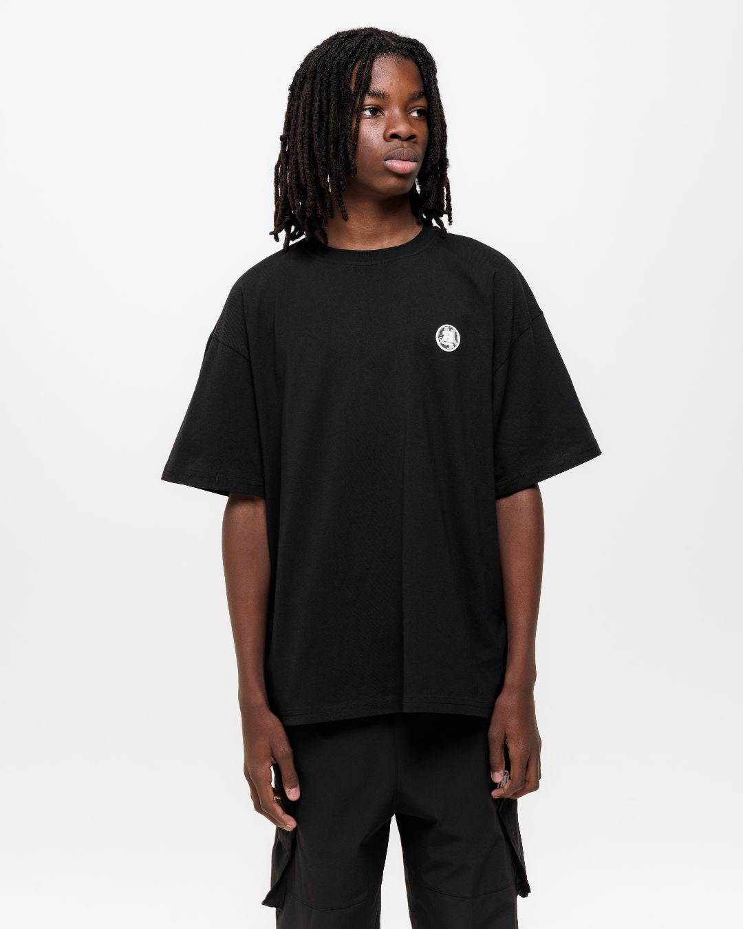 boy wearing next gen black junior oversized t-shirt and cargo pants with Rascal camo logo design stood in front of a white background