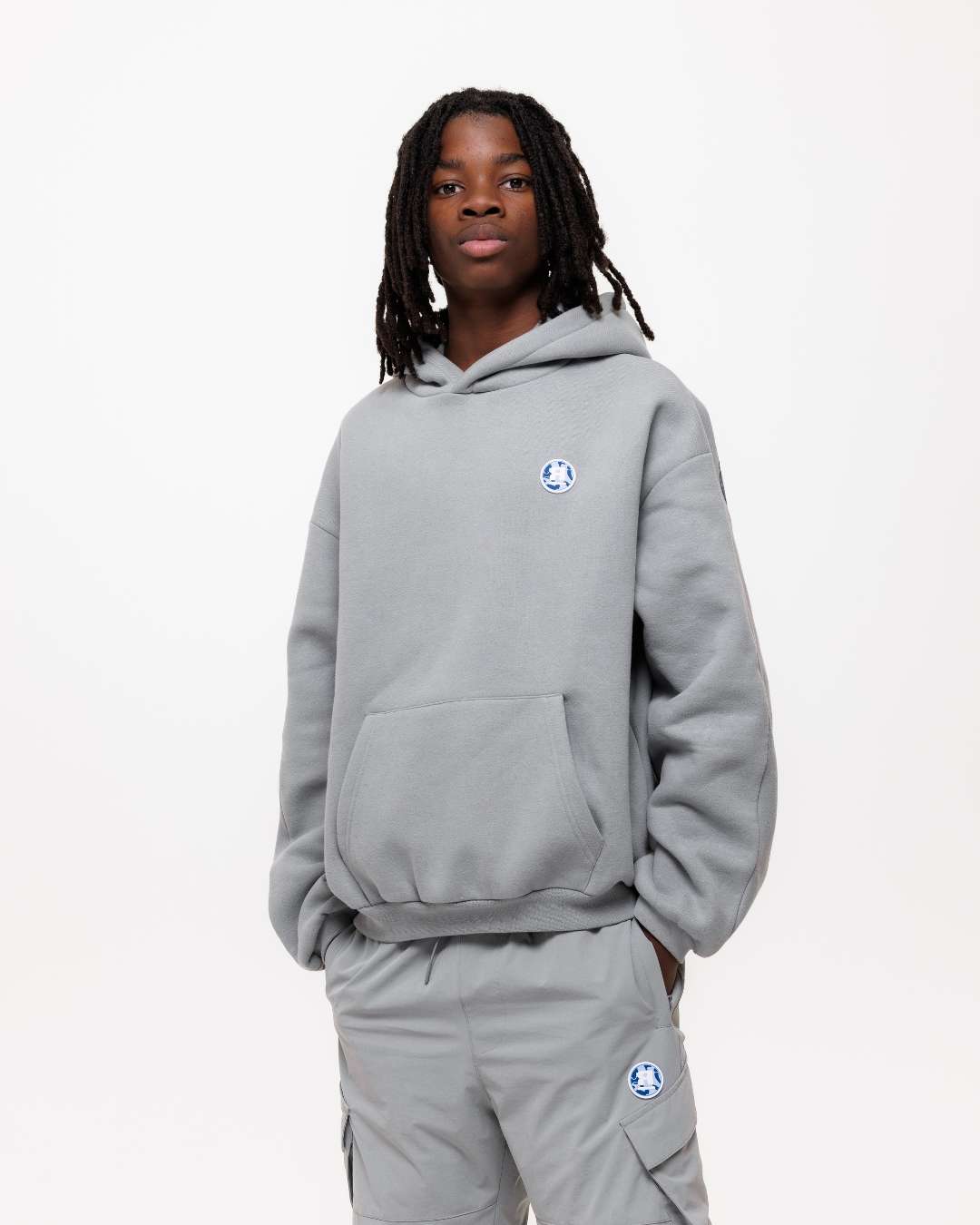 boy wearing next gen junior grey oversized hoodie and cargo pants with Rascal camo logo designs, stood in front of a white background and hands in pockets