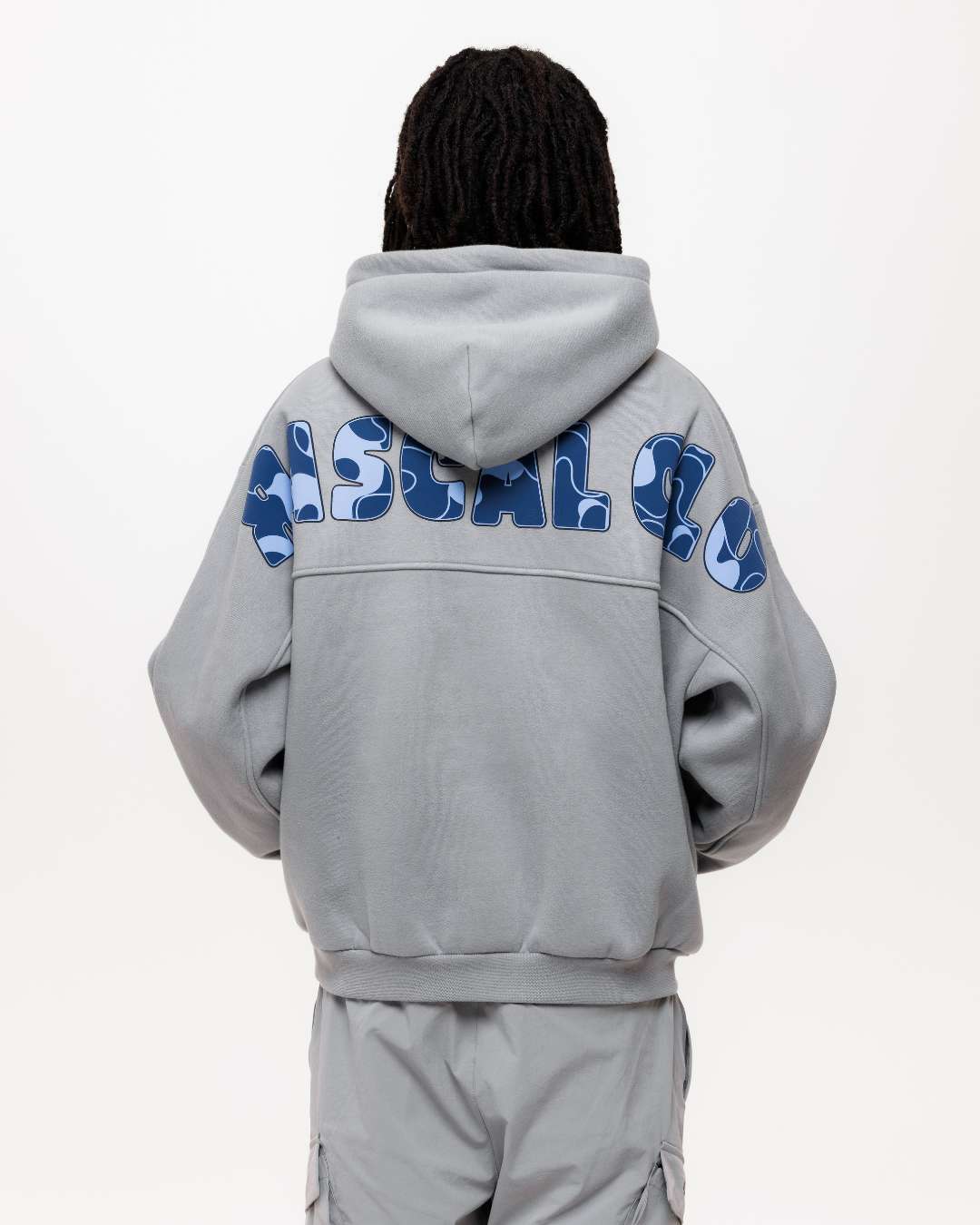 boy wearing next gen junior grey oversized hoodie and with Rascal camo text design across the back, stood in front of a white background and hands in kangaroo pocket