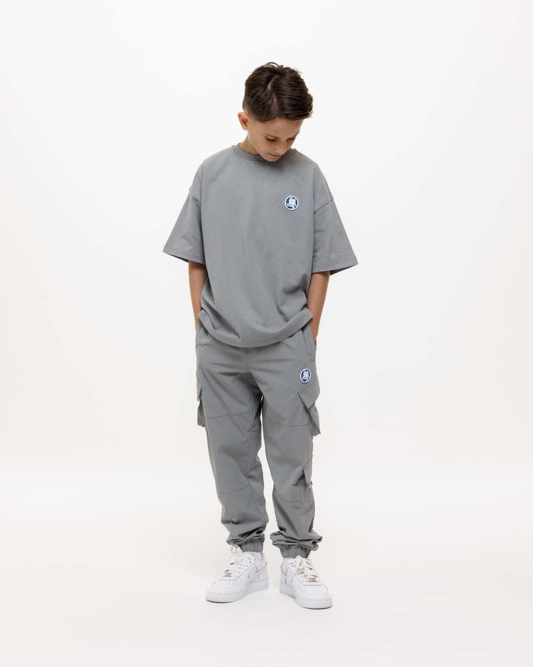 boy wearing next gen junior grey oversized tee and cargo pants looking down at Rascal camo logo design, stood in front of a white background and hands in pockets