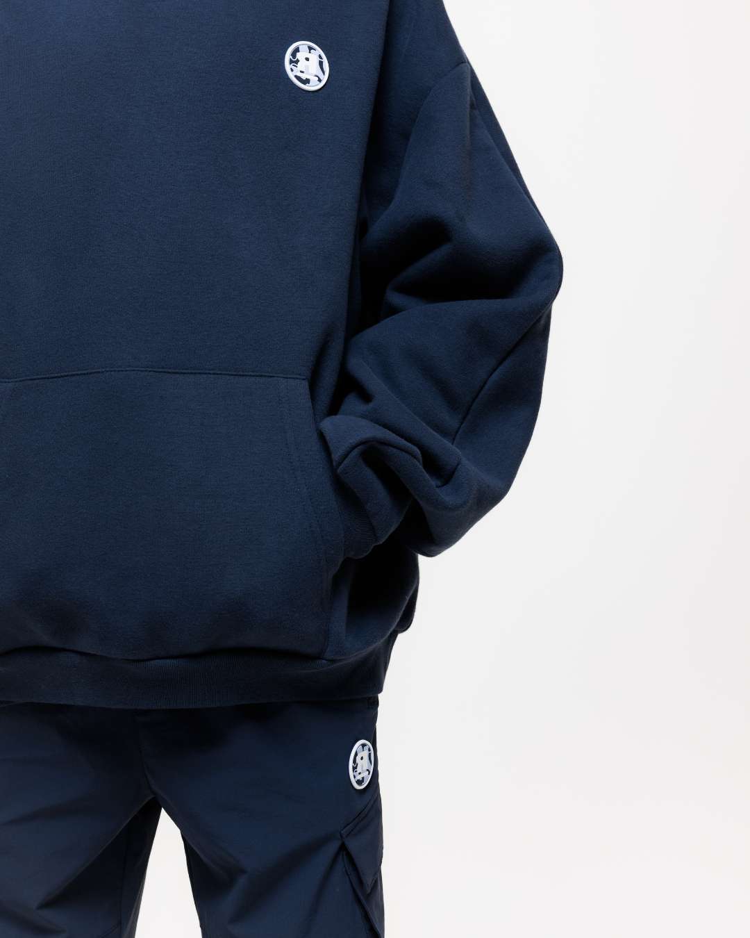 close up of next gen navy blue junior oversized hoodie with Rascal camo logo designs and hands in kangaroo pocket against a white background