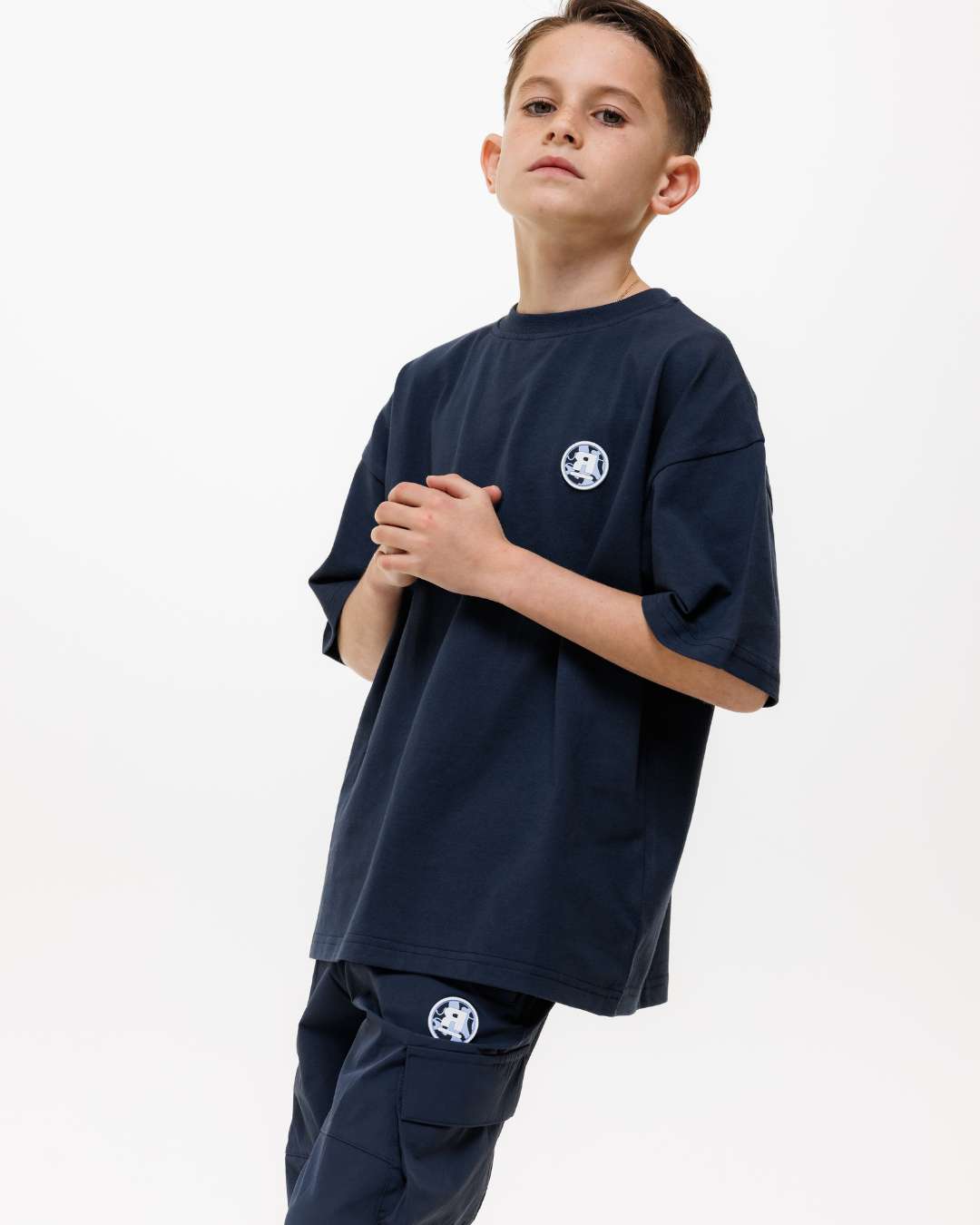 boy wearing next gen navy blue junior t-shirt and cargo pants with Rascal camo logo text designs stood in front of a white background