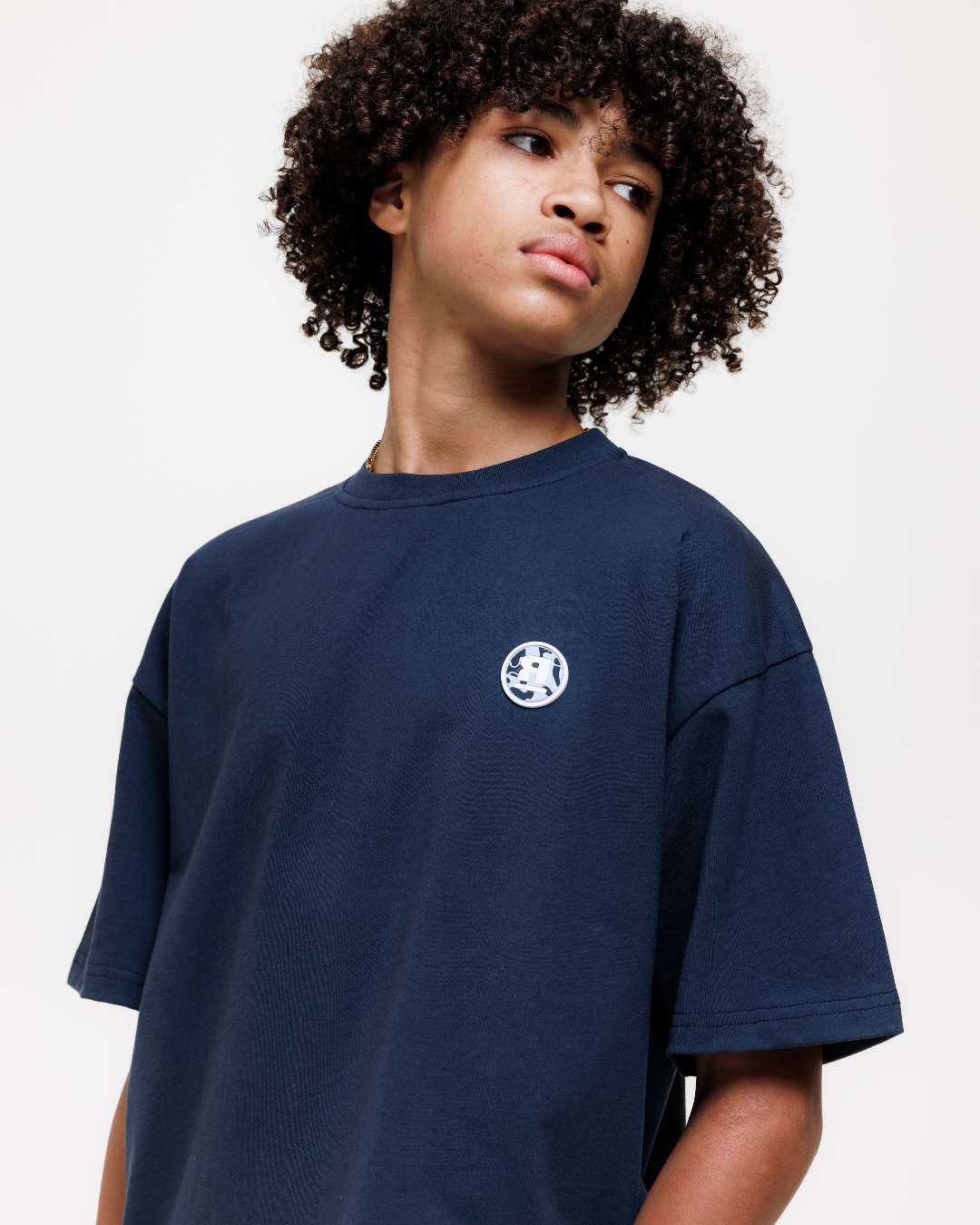 close up of boy wearing next gen navy blue junior oversized t-shirt with Rascal camo logo designs stood in front of a white background