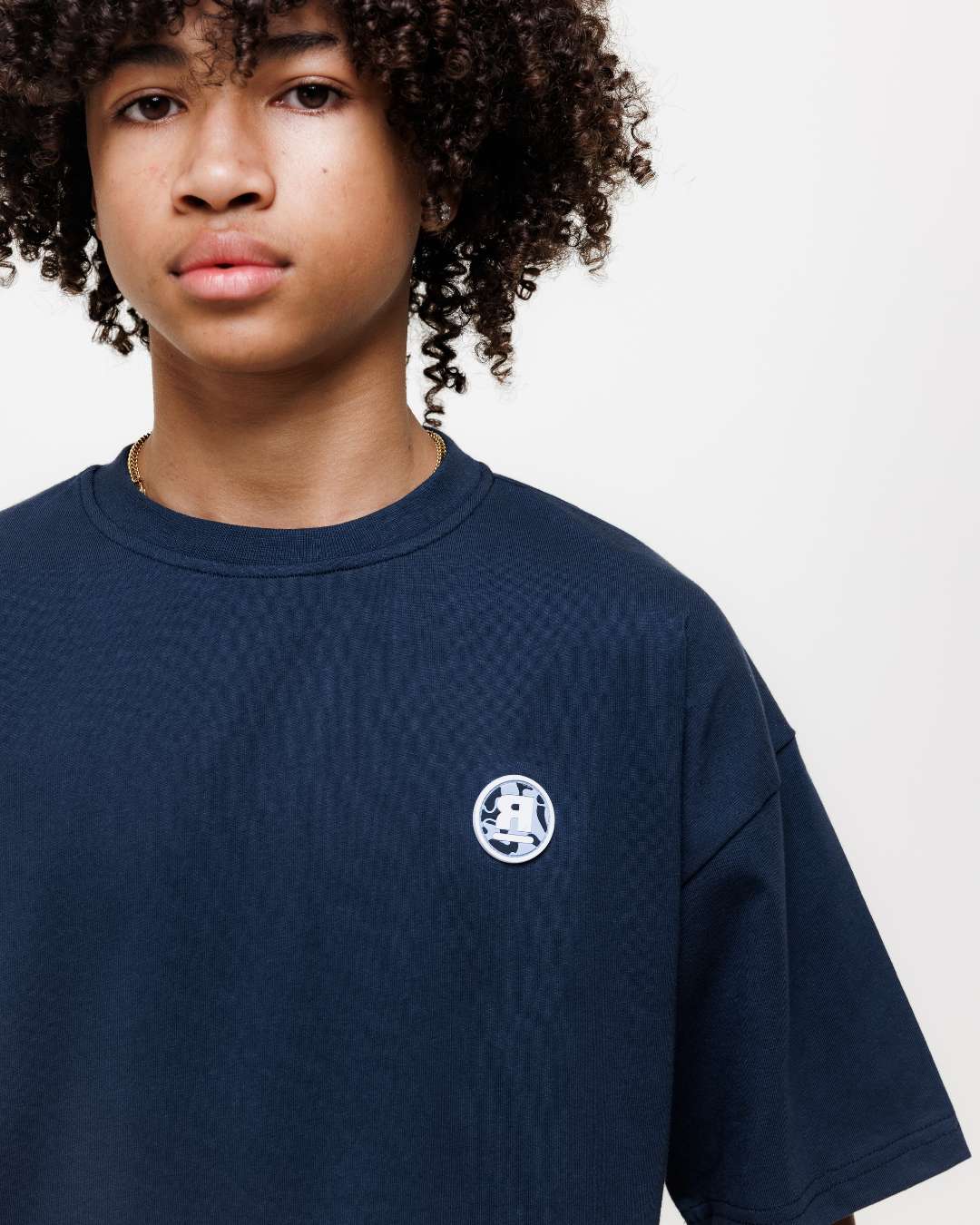 boy wearing next gen navy blue junior oversized t-shirt with Rascal camo logo design stood in front of a white background