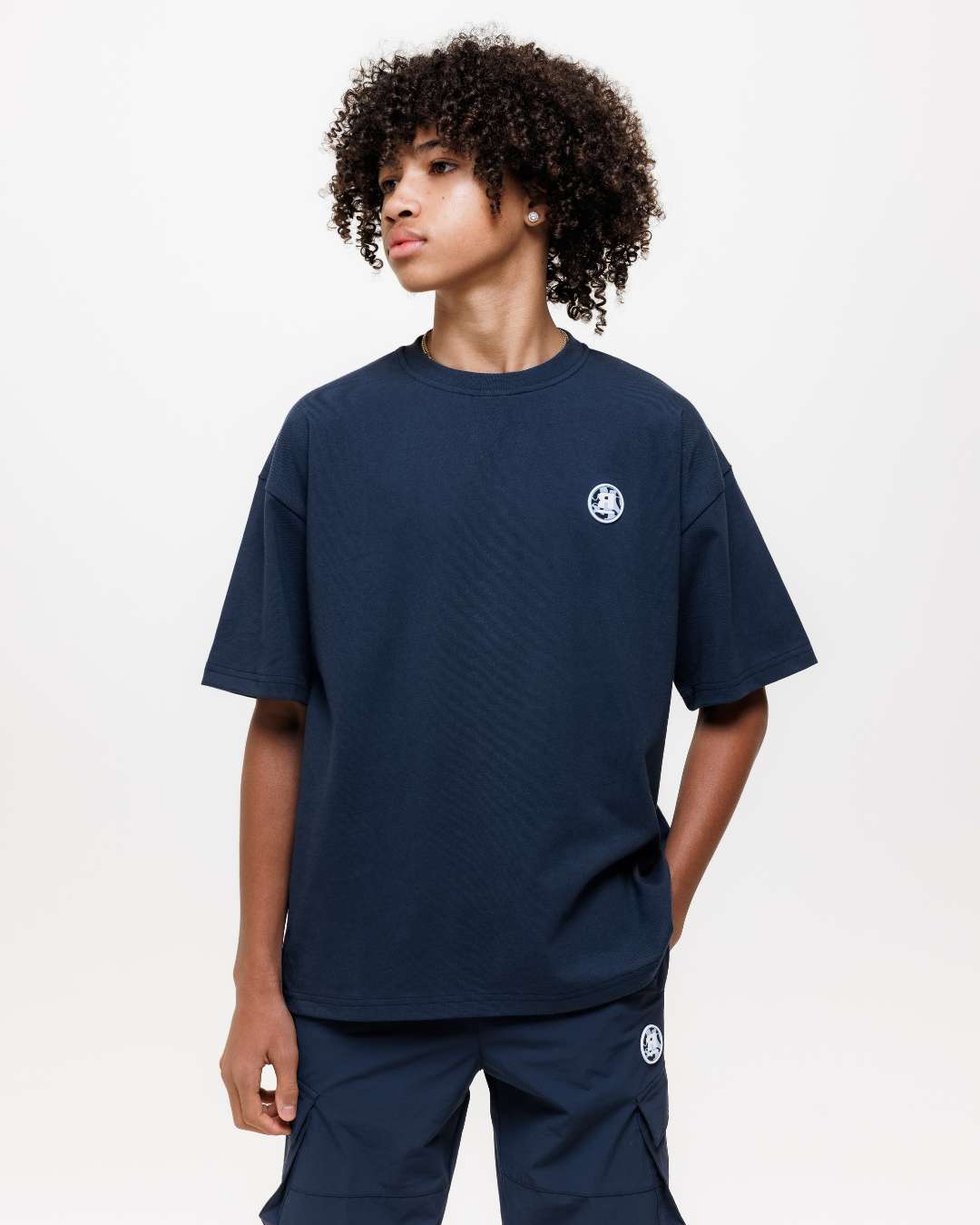 boy wearing next gen navy blue junior oversized t-shirt and cargo pants with Rascal camo logo designs, hand in pocket stood in front of a white background